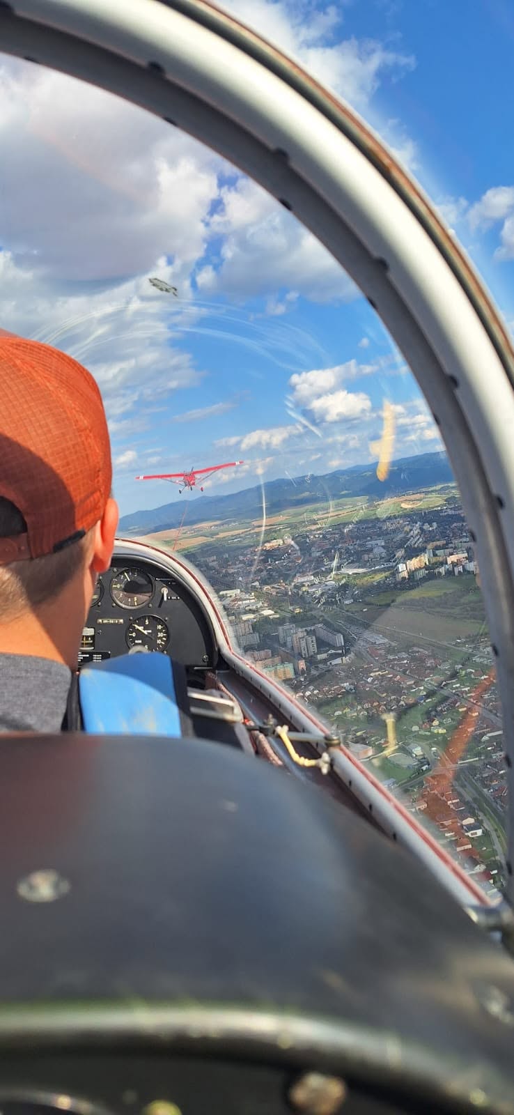 Pohľad z vetroňa počas aerovleku za červeným vlečným lietadlom nad mestom