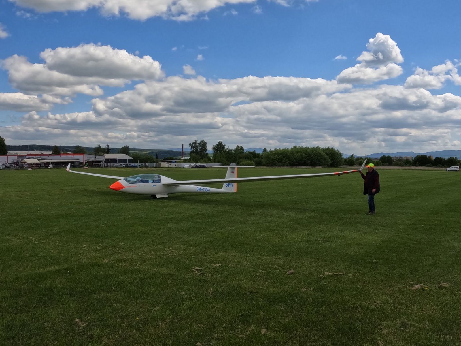 Vetroň Duo Discus XT OM-1954 na tráve letiska, pomocník drží koniec krídla