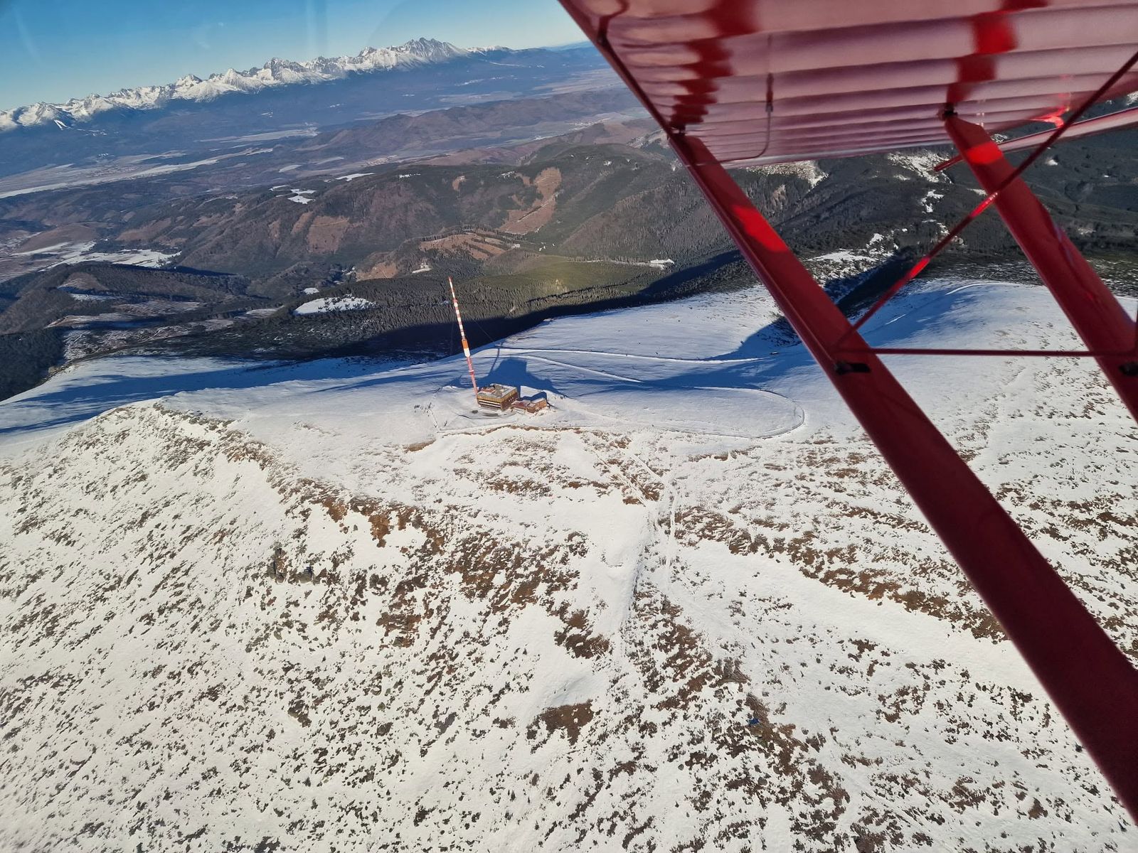Vysielač na zasneženom hrebeni pod krídlom lietadla, v pozadí Vysoké Tatry